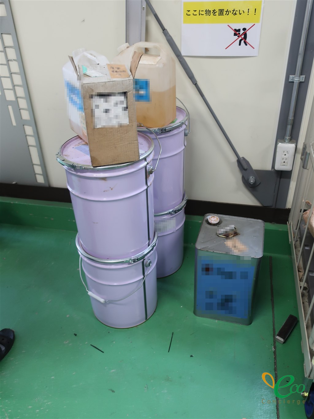「ここに物を置かない!!」の貼り紙の前に、油の入ったペール缶とポリタンクが置かれている様子