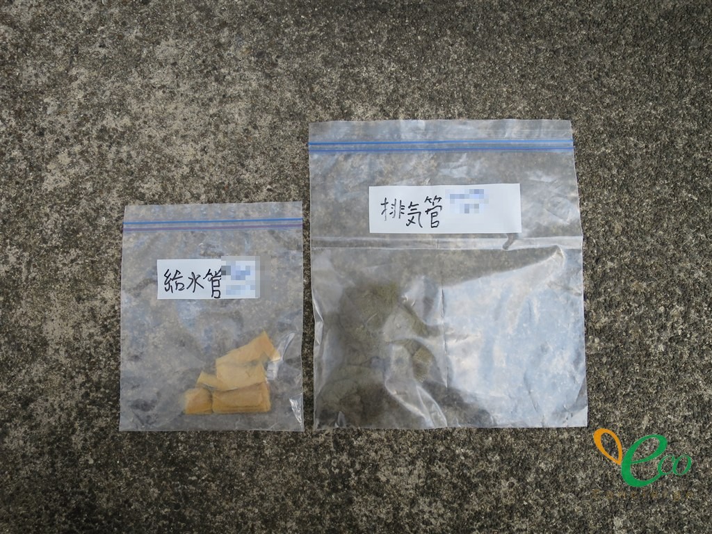 灰色のざらついた床の上に並べられた2つの透明な袋。それぞれに「給水管」「排気管」と手書きされている