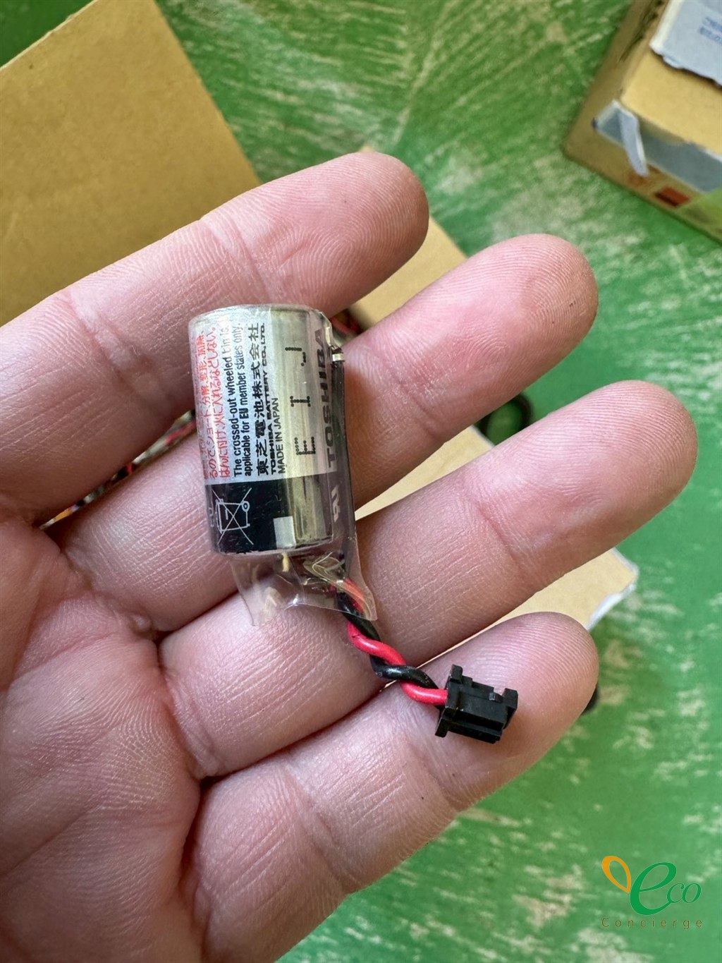 手のひらに載せた、リード線とコネクタの付いた小型の電池1個