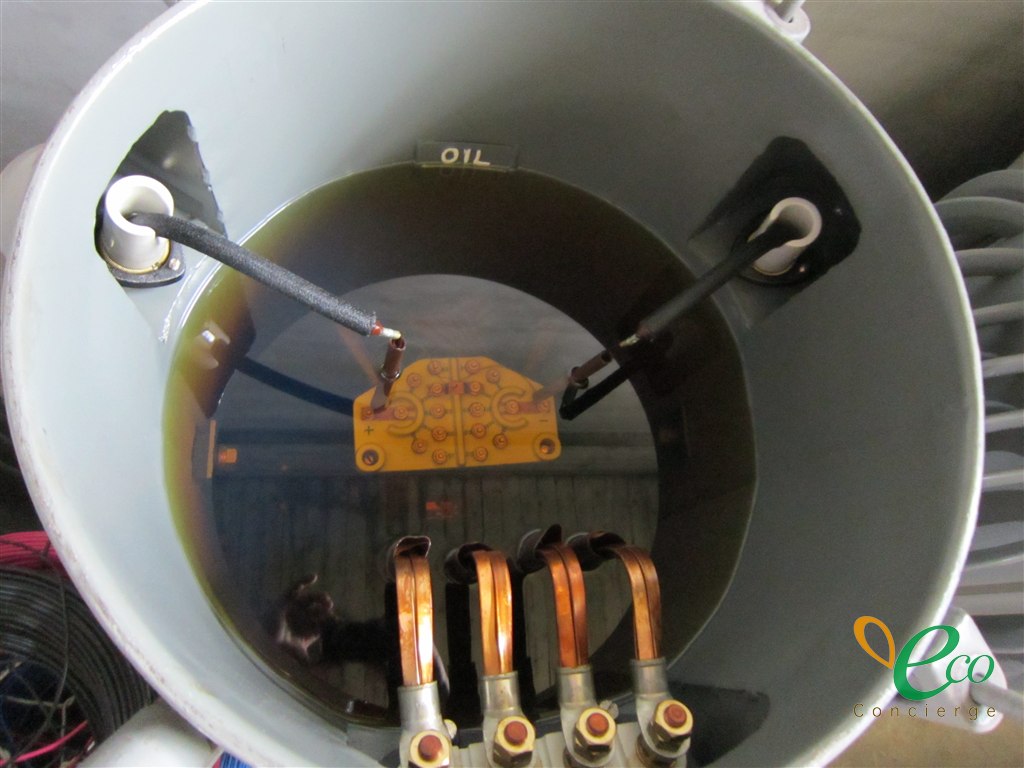 油入りの電気機器の点検口を上から見たところ。内部に黄褐色の絶縁油が見え、油面に周囲が映り込んでいる