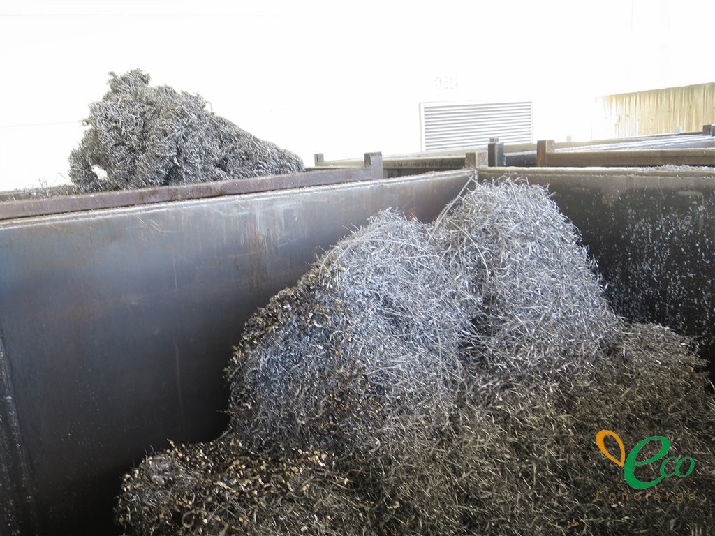 複数の鉄製コンテナが並び、手前のコンテナに、黒っぽい細かい切削くずと銀色の線状の切削くずが混ざった山が積まれている様子