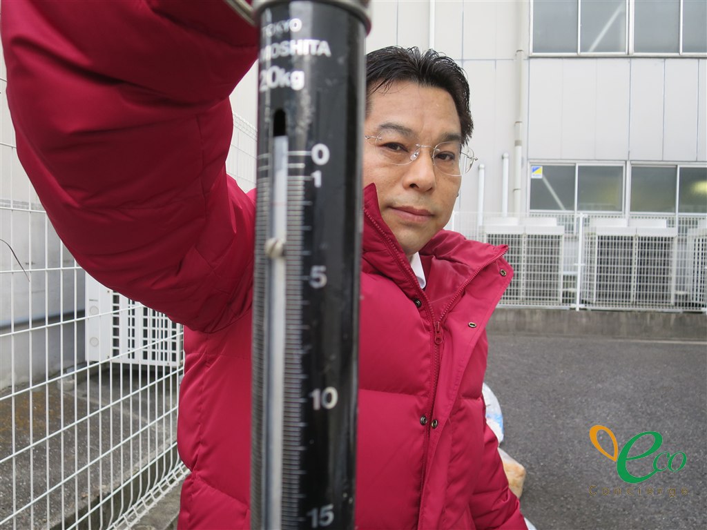 吊り下げ式の秤の目盛り部分を近くから写した様子。担当者が目盛りを読み取っている