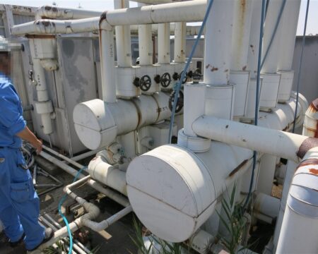 屋上の冷温水配管設備を作業員が点検している様子