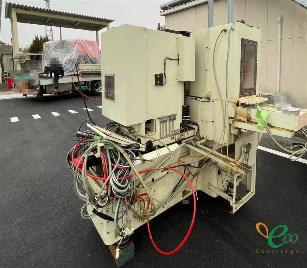 屋外の舗装の上に置かれたクリーム色の機械。赤いホースや電線がついたまま束ねてある