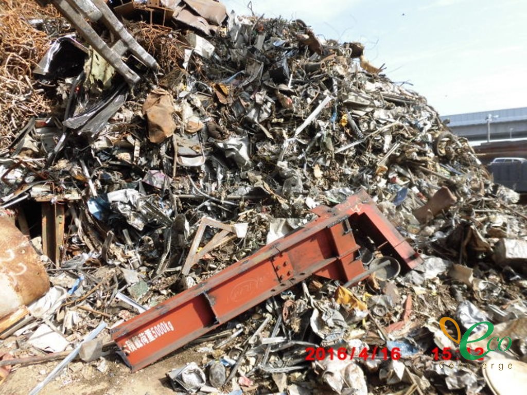 様々な金属くずが山のように積み上げられ、赤い鉄骨部材が上に乗っている様子